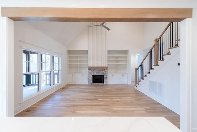 unfurnished living room featuring visible vents, stairs, light wood-style floors, built in shelves, and beam ceiling