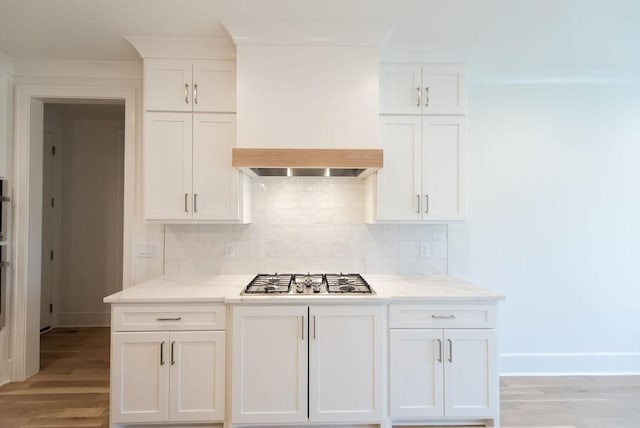 kitchen with light wood finished floors, tasteful backsplash, white cabinets, premium range hood, and stainless steel gas cooktop