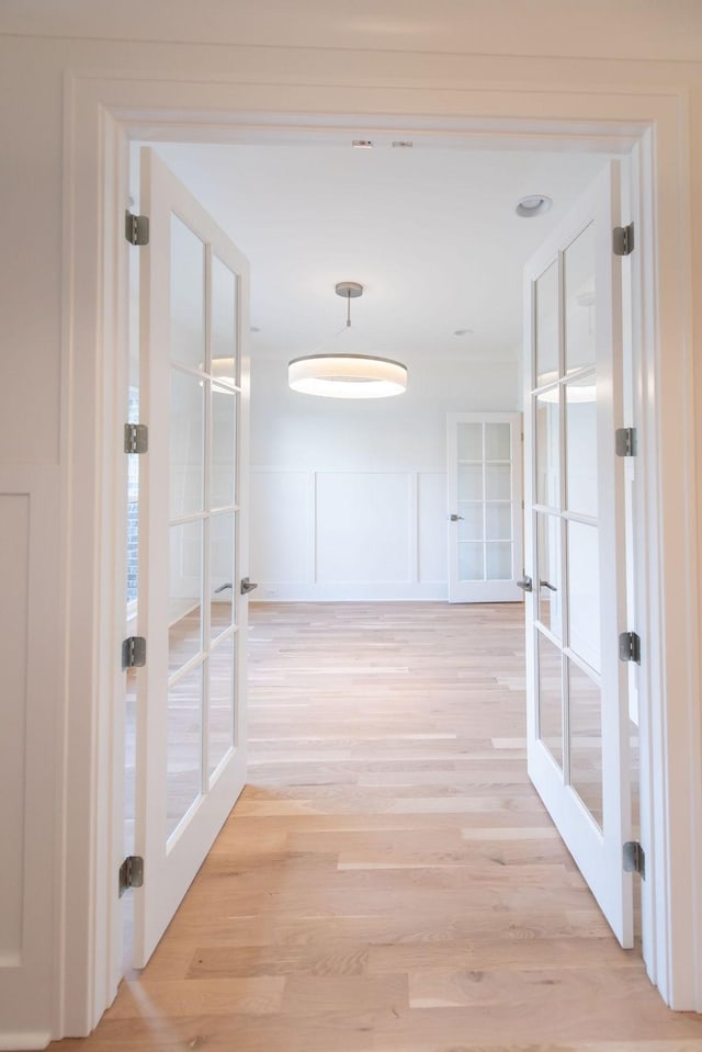 corridor featuring light wood finished floors, french doors, and a decorative wall