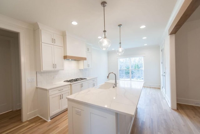 kitchen with stainless steel gas stovetop, premium range hood, a sink, and white cabinetry