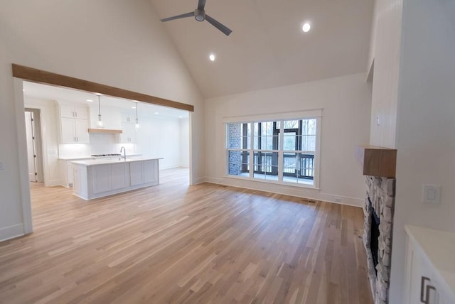 unfurnished living room with ceiling fan, high vaulted ceiling, a fireplace, and light wood-style floors
