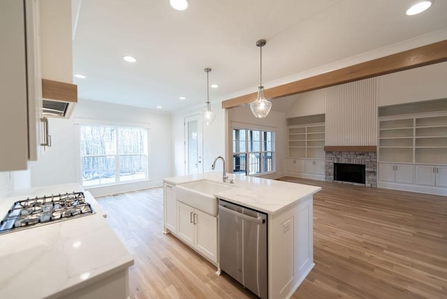 kitchen with light stone counters, stainless steel appliances, a sink, open floor plan, and light wood finished floors