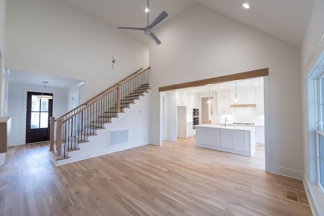 unfurnished living room featuring light wood-style flooring, visible vents, a sink, and stairway