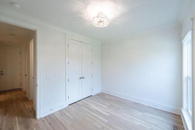unfurnished bedroom featuring light wood-style floors, a closet, crown molding, and baseboards