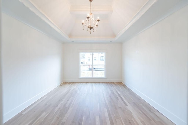 spare room featuring a tray ceiling, light wood-style flooring, vaulted ceiling, a chandelier, and baseboards