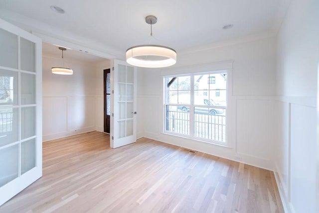 empty room with light wood-type flooring, french doors, wainscoting, and a decorative wall