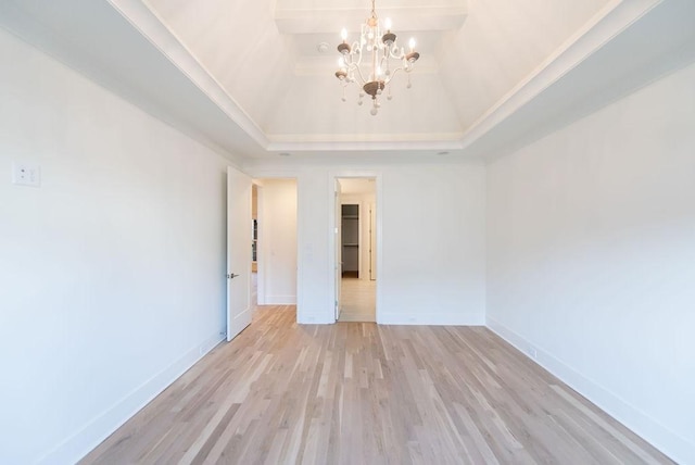 empty room with a notable chandelier, light wood finished floors, and baseboards