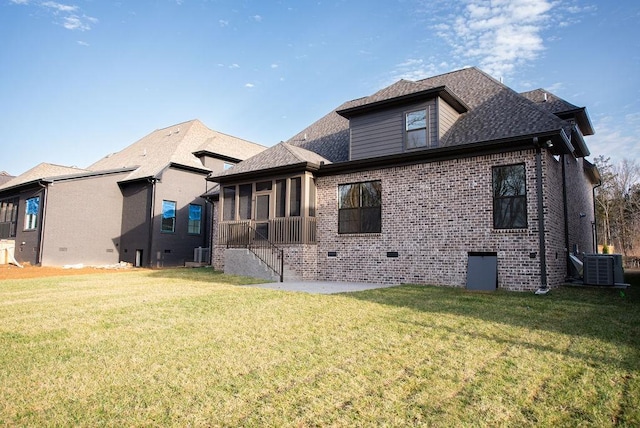 rear view of property with a sunroom, brick siding, a lawn, and central air condition unit