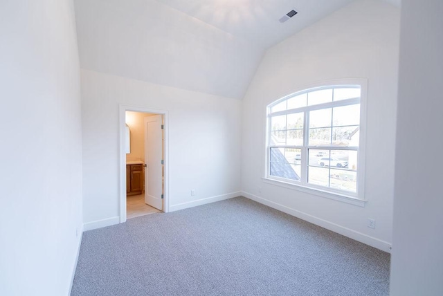 empty room featuring light colored carpet, vaulted ceiling, visible vents, and baseboards