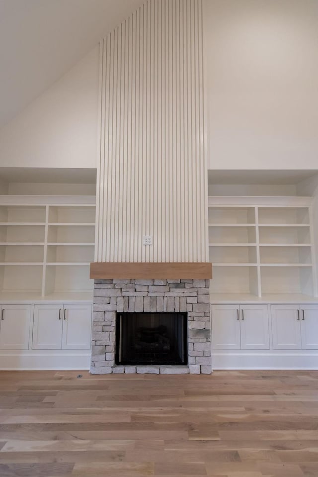 unfurnished living room with lofted ceiling, light wood-type flooring, and a stone fireplace