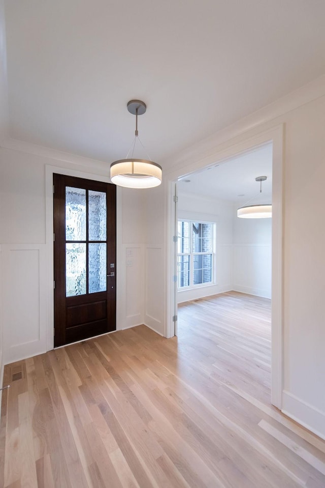 entrance foyer with light wood finished floors, a decorative wall, and wainscoting