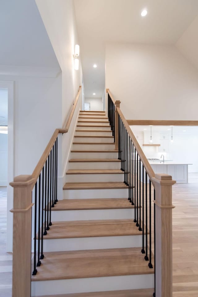 stairway with a high ceiling, wood finished floors, and recessed lighting