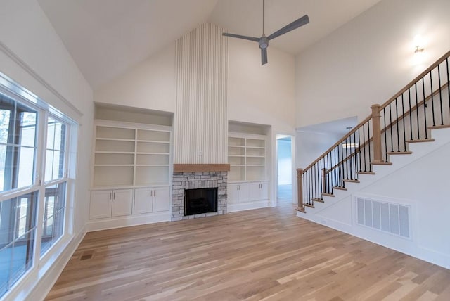 unfurnished living room with visible vents, stairway, light wood-type flooring, built in shelves, and high vaulted ceiling