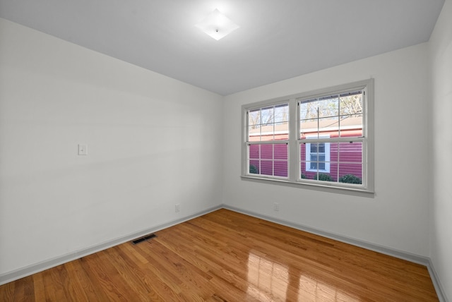 empty room with visible vents, light wood-style flooring, and baseboards