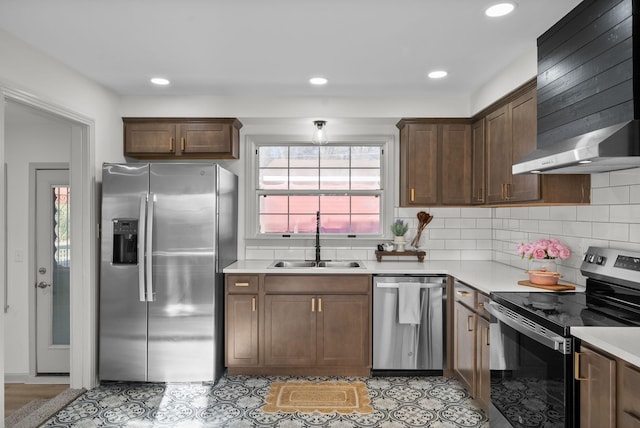 kitchen with appliances with stainless steel finishes, light countertops, a sink, and wall chimney exhaust hood