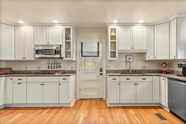 kitchen featuring light wood-type flooring, appliances with stainless steel finishes, white cabinets, and a sink