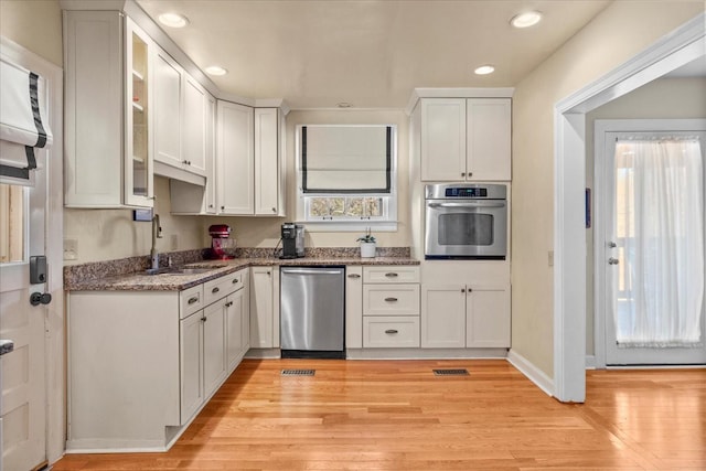 kitchen featuring appliances with stainless steel finishes, glass insert cabinets, white cabinetry, a sink, and light wood-type flooring