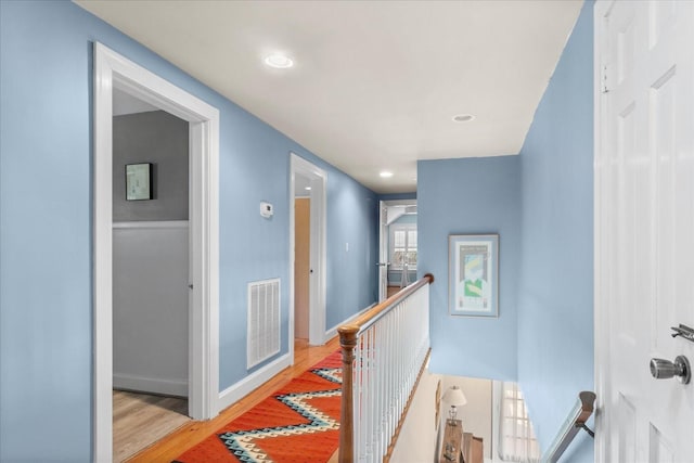 hallway featuring visible vents, wood finished floors, an upstairs landing, and baseboards