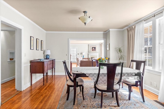 dining room with ornamental molding, a fireplace, and light wood finished floors