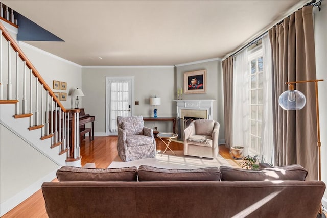 living room featuring a fireplace with flush hearth, wood finished floors, baseboards, ornamental molding, and stairway