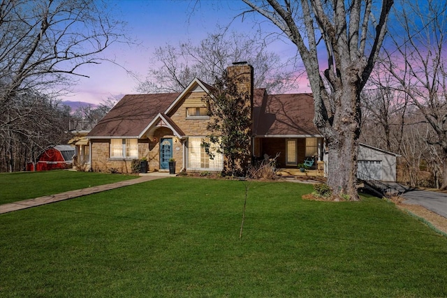 view of front of property featuring stone siding, a yard, and a chimney