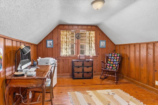 office area featuring lofted ceiling, wood walls, light wood-style flooring, and a textured ceiling