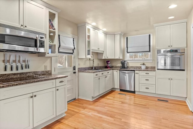 kitchen with stainless steel appliances, a sink, white cabinetry, light wood-type flooring, and dark stone countertops