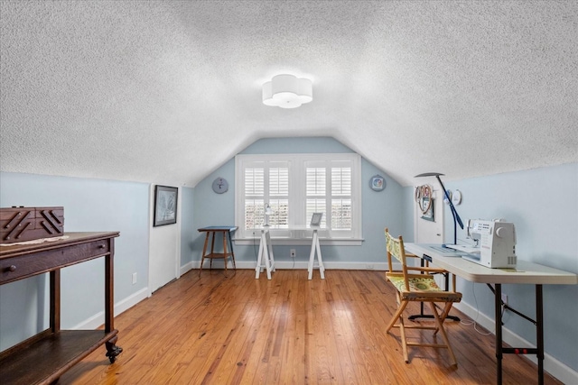 office space with vaulted ceiling, hardwood / wood-style floors, a textured ceiling, and baseboards