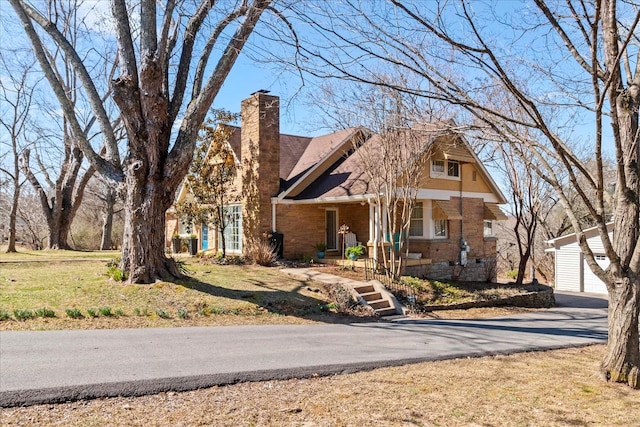 view of front facade with an outbuilding, brick siding, a chimney, covered porch, and a front lawn