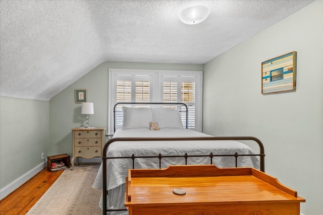 bedroom with lofted ceiling, a textured ceiling, baseboards, and wood finished floors