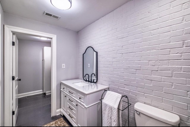 half bath with toilet, brick wall, vanity, visible vents, and baseboards