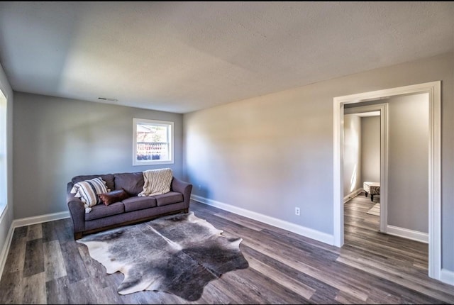 living area with dark wood-type flooring, a textured ceiling, and baseboards