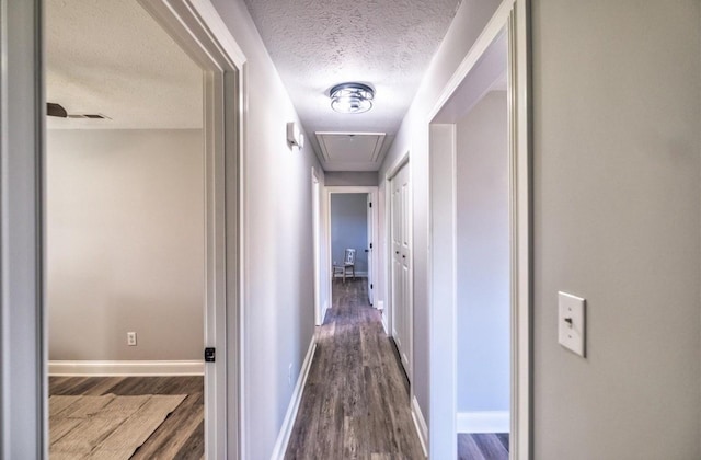 hallway with attic access, visible vents, baseboards, dark wood-style floors, and a textured ceiling