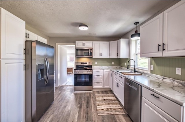 kitchen featuring white cabinets, dark wood-style floors, appliances with stainless steel finishes, pendant lighting, and a sink