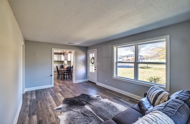 living room with a textured ceiling, dark wood-style flooring, and baseboards