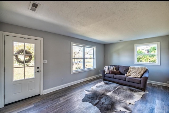 living area featuring a textured ceiling, dark wood-type flooring, visible vents, and baseboards