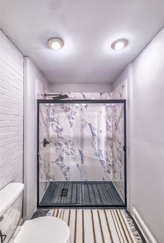 full bathroom featuring brick wall, a marble finish shower, toilet, and baseboards