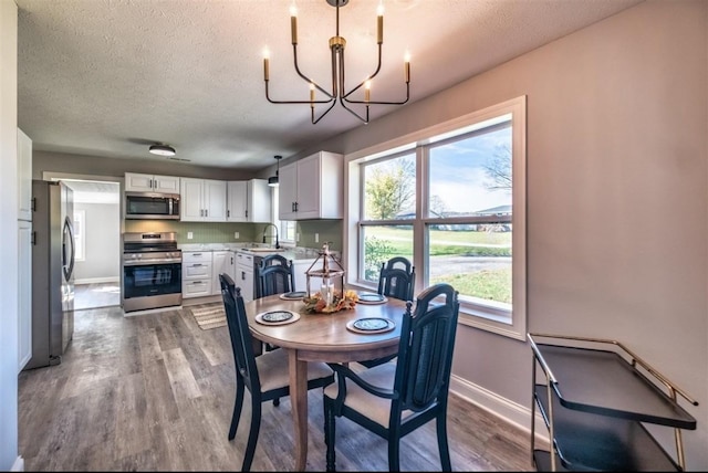 dining area with an inviting chandelier, a textured ceiling, baseboards, and wood finished floors