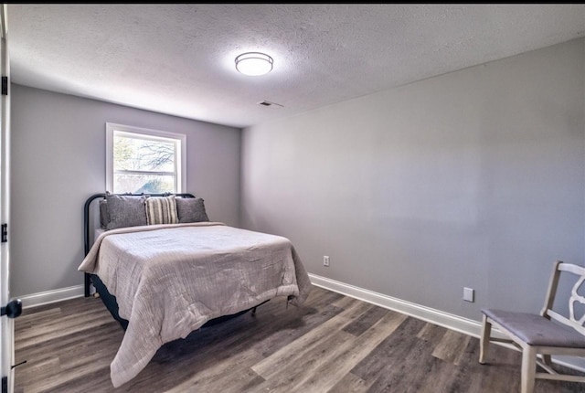 bedroom with a textured ceiling, wood finished floors, visible vents, and baseboards