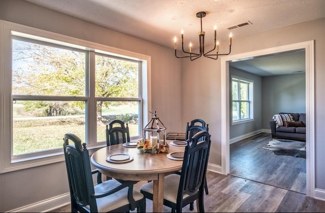 dining area featuring a textured ceiling, a notable chandelier, visible vents, baseboards, and dark wood finished floors