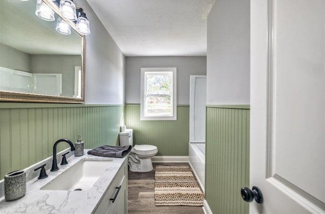 bathroom with a wainscoted wall, toilet, a textured ceiling, vanity, and wood finished floors