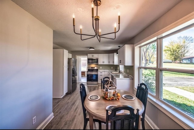 dining area featuring a textured ceiling, baseboards, wood finished floors, and an inviting chandelier