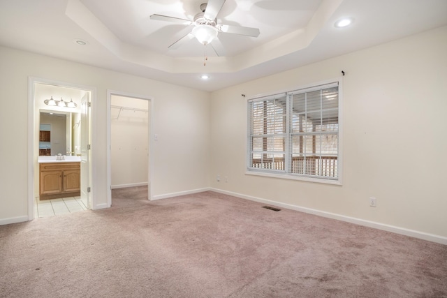 unfurnished bedroom with a raised ceiling, light carpet, a spacious closet, and baseboards