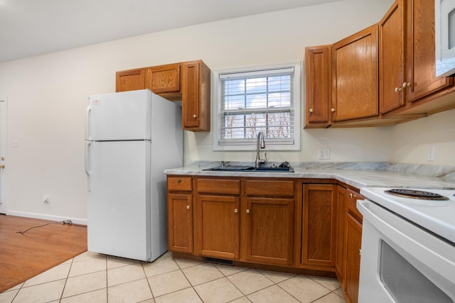 kitchen featuring light tile patterned floors, white appliances, a sink, light countertops, and brown cabinetry