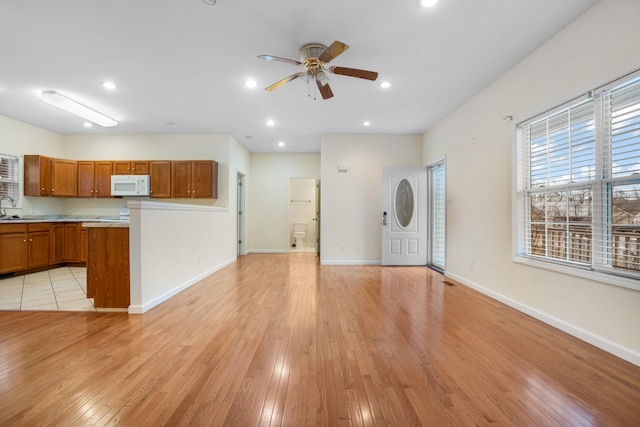 kitchen featuring baseboards, brown cabinetry, white microwave, light wood-style floors, and a sink