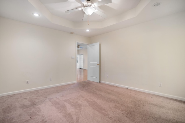 spare room with light carpet, ceiling fan, baseboards, and a raised ceiling