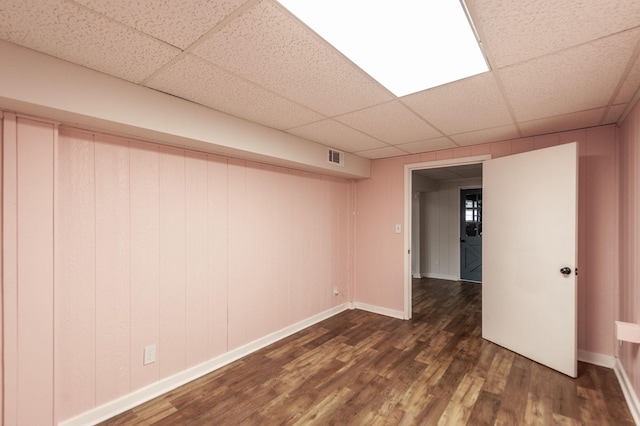 finished below grade area featuring dark wood-type flooring, a paneled ceiling, and baseboards