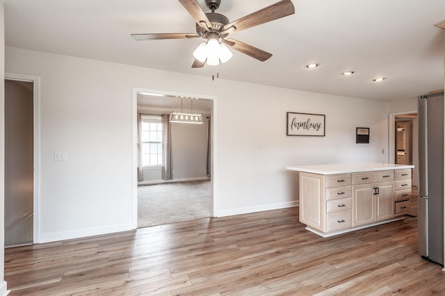 kitchen with a center island, light wood finished floors, light countertops, a ceiling fan, and baseboards