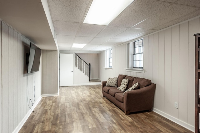 living room featuring a paneled ceiling, baseboards, stairway, and wood finished floors