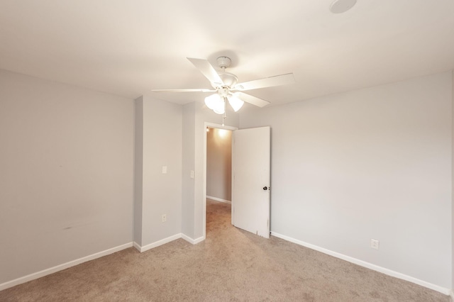 spare room with a ceiling fan, light colored carpet, and baseboards